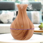 Wood grain aroma diffuser with visible vapor/mist and blue LED light band, light brown.
