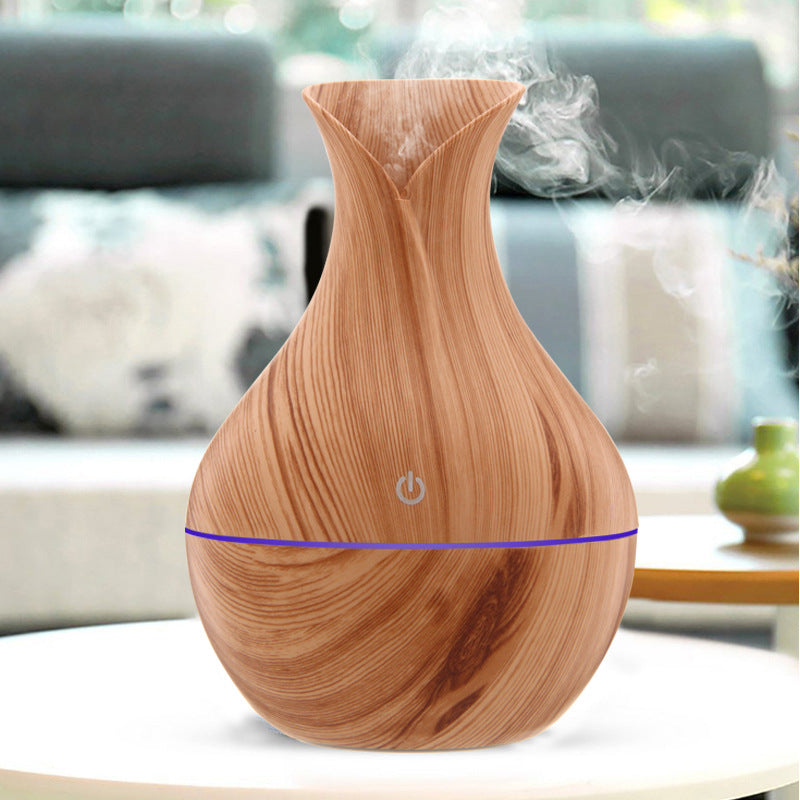 Wood grain aroma diffuser with visible vapor/mist and blue LED light band, light brown.