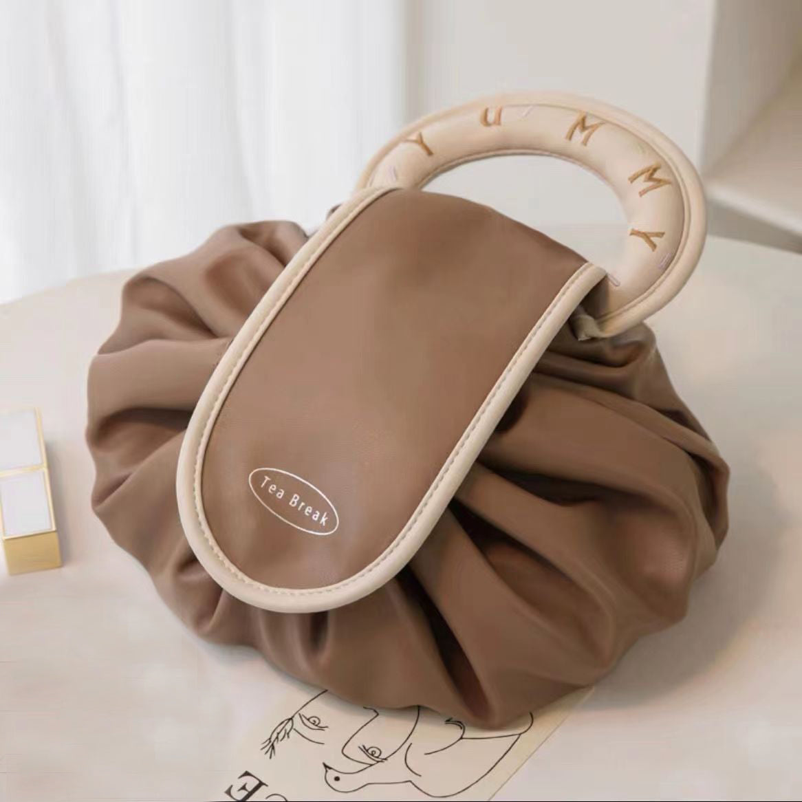Beige drawstring wash bag with round-lettered handle and Tea Break patch