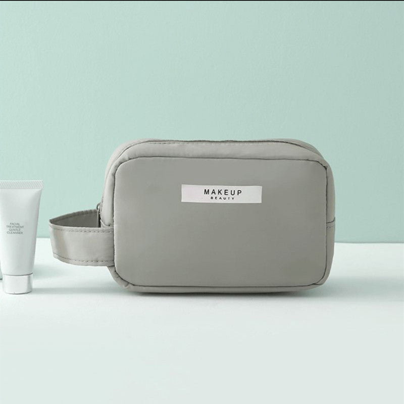 Light gray compact makeup travel pouch with front label and zip closure