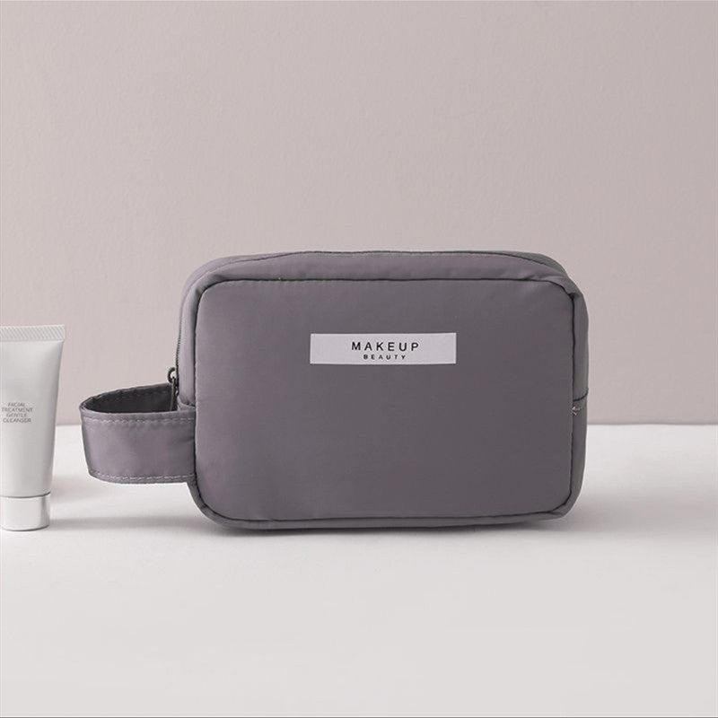 Dark gray compact makeup travel pouch with front label and zip closure