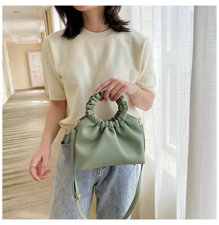 Cream crossbody travel bag held up; ruched drawstring top and crossbody strap