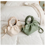 Green crossbody travel bag with ruched top and strap beside a cream bag