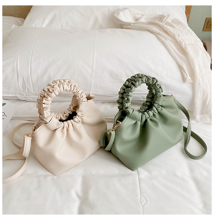 Green crossbody travel bag with ruched top and strap beside a cream bag