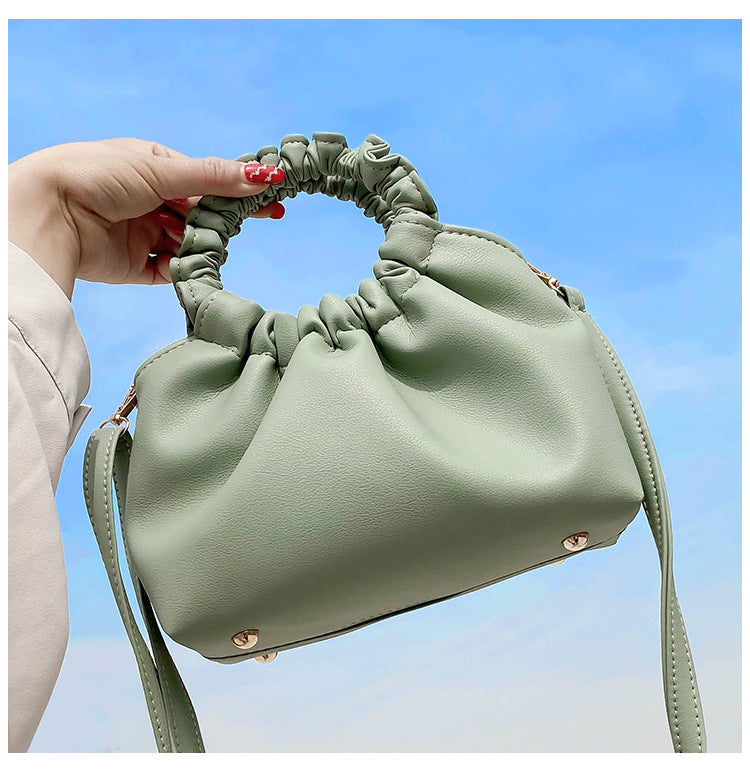 Light green crossbody travel bag with ruched handle, gold hardware, and long strap