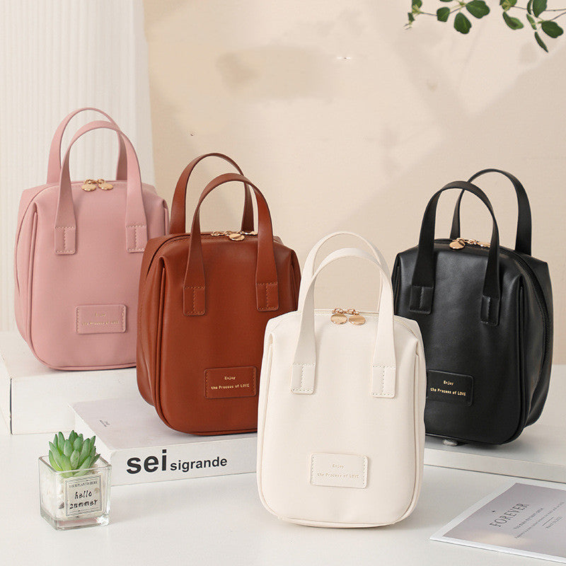 Set of travel vanity bags in pink, brown, white, and black with top handles.