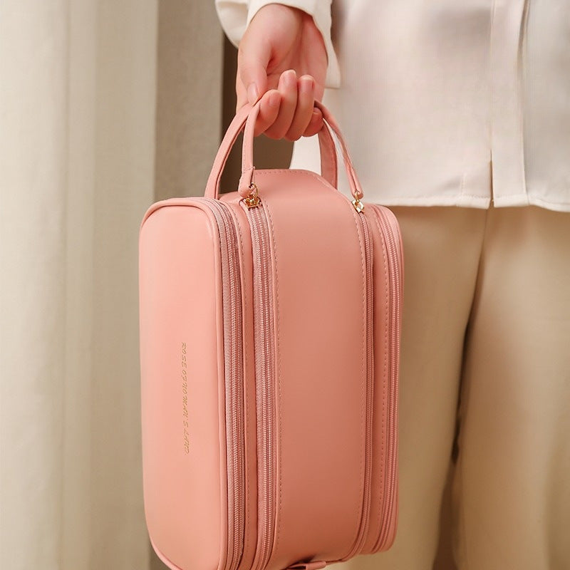 Pink travel vanity case held by its handle, zip front, slim side pockets