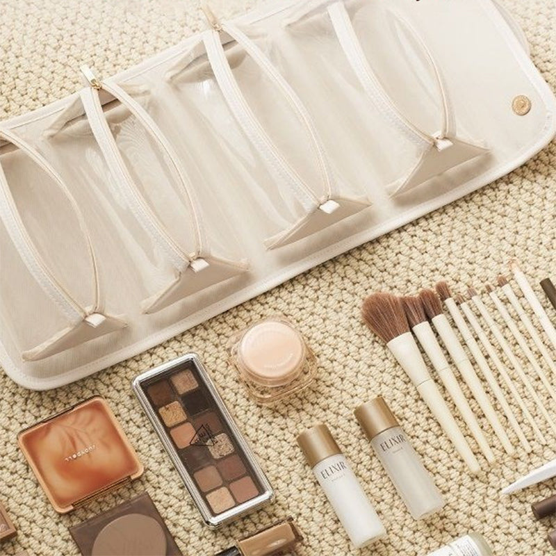 Light beige folding vanity bag laid open with clear compartments and elastic brush slots.
