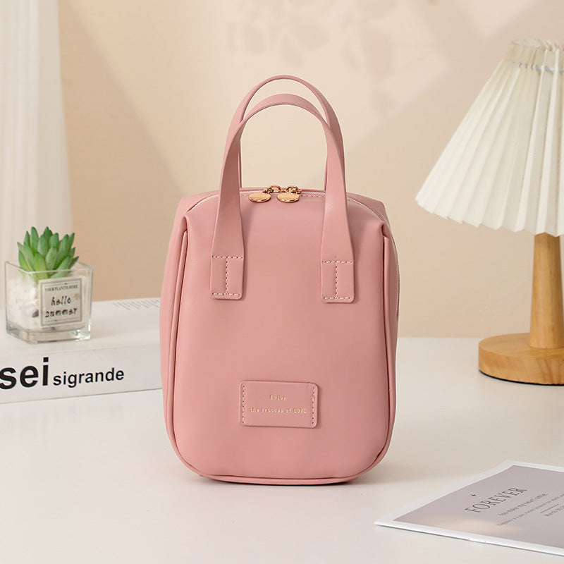 Pink travel vanity bag with top handles and front logo patch.