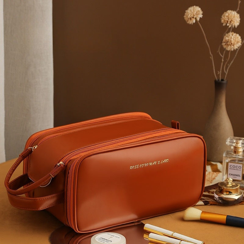 Orange-brown structured travel vanity case with zip, crossbody strap, and front monogram