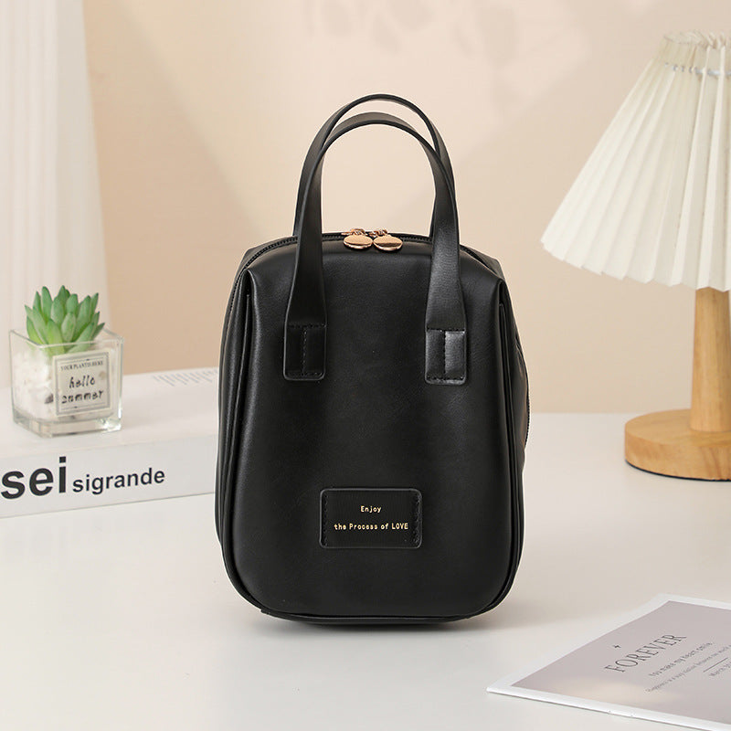 Black travel vanity bag with top handles and front logo patch.