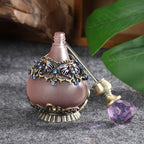 Perfume oil bottle with mauve glass body, blue floral metal trim, and purple stopper