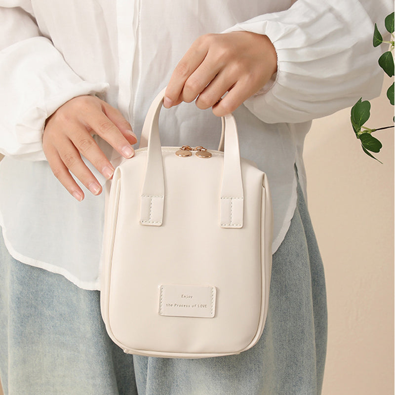 White travel vanity bag with top handles, stitched panels, and front logo patch.