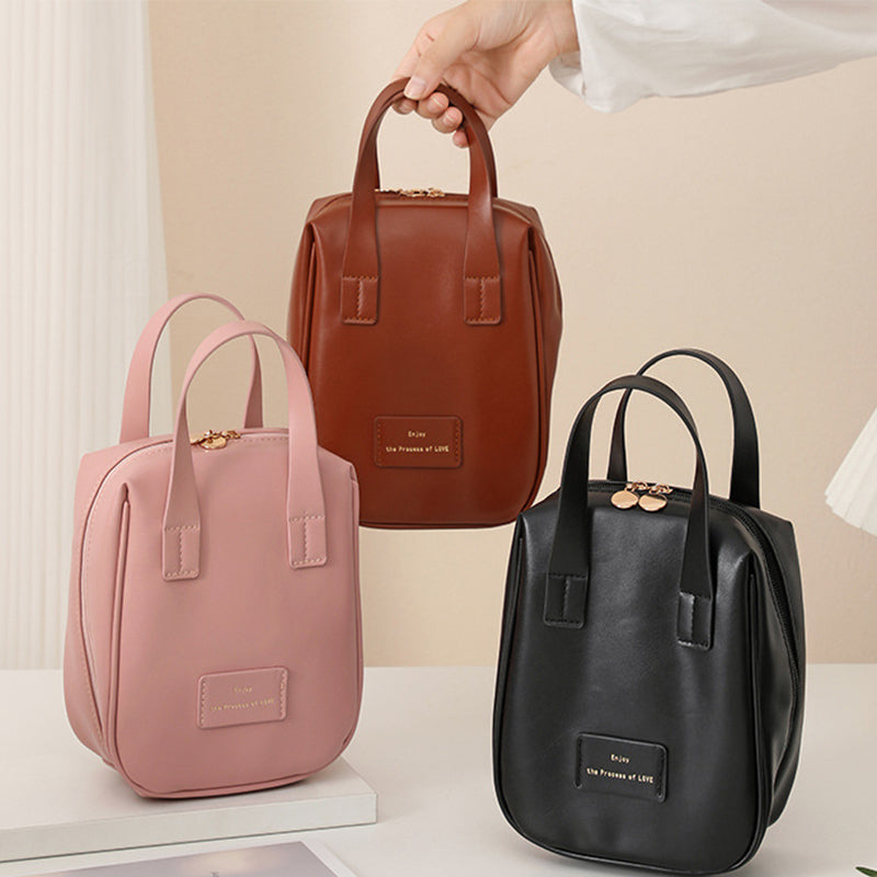 Travel vanity bags in pink, brown, and black, each with top handles and front label.
