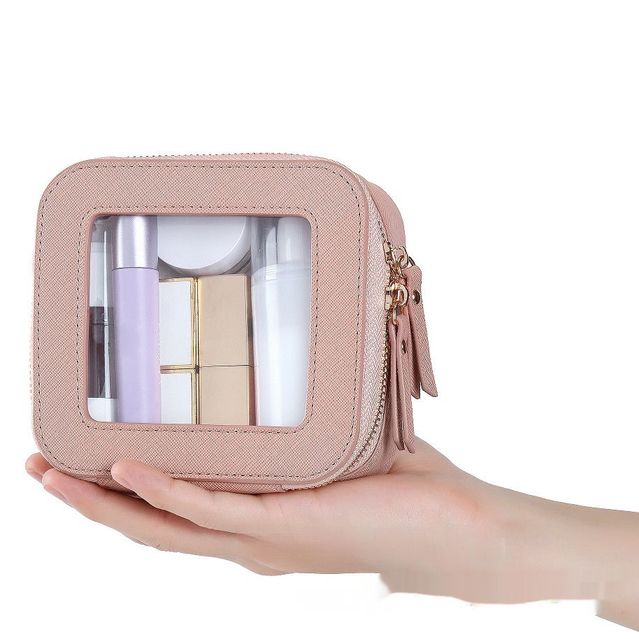 Light pink clear cosmetic pouch with gold zipper and clear window, held in hand