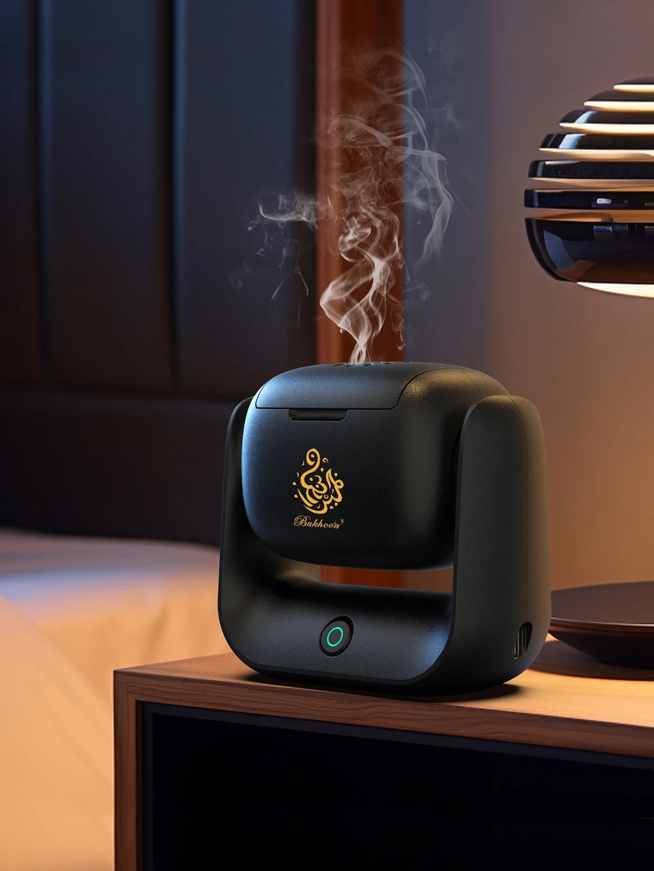 Black bakhoor burner emitting incense smoke, gold logo on front