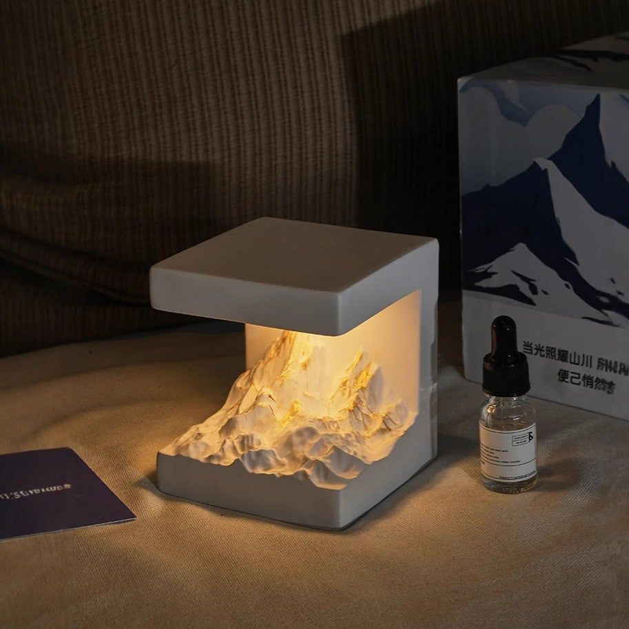 Gray cube aromatherapy lamp with warm glow and amber essential oil bottle