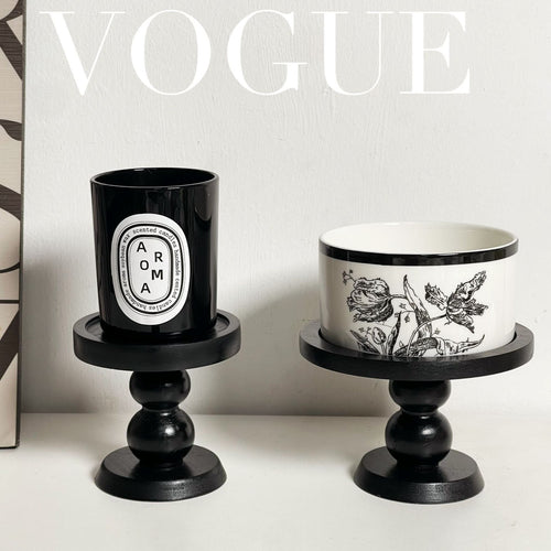 Black scent trays on pedestal bases holding two candle cups, one patterned