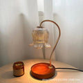 Aroma diffuser with bell-shaped glass shade glowing warm; amber candle jar beside base