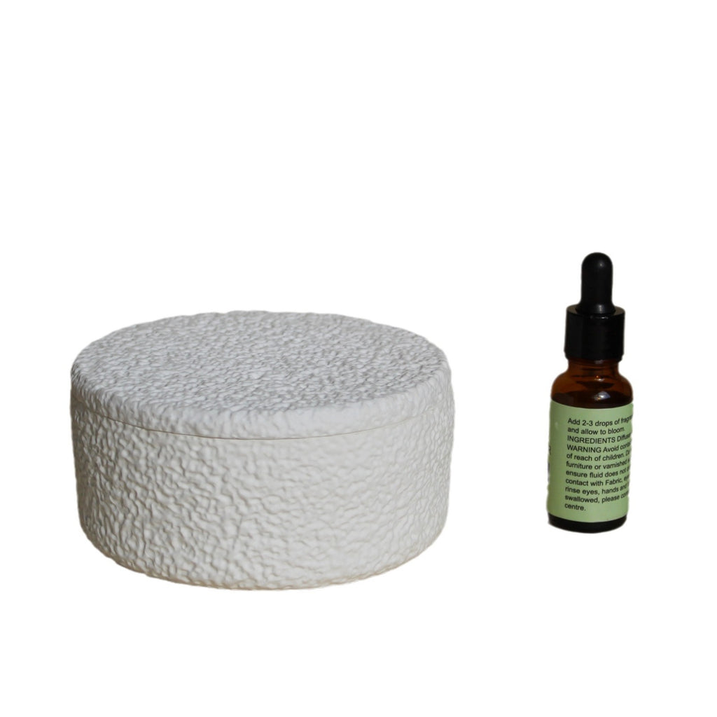 White textured diffuser with gray round lid and essential oil bottle beside it