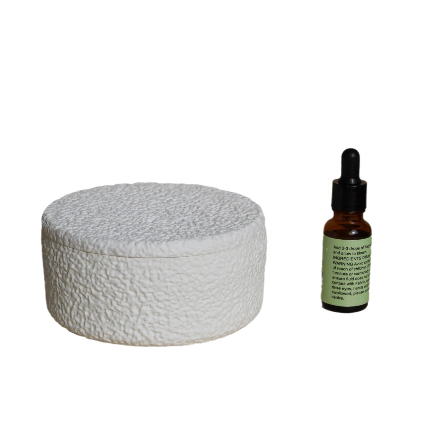 White textured diffuser with gray round lid and essential oil bottle beside it
