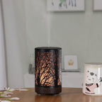 Mini aroma diffuser with dark base, warm amber forest glow, round top vent holes