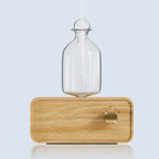 Essential oil diffuser with clear glass bottle on light wood base and round power dial