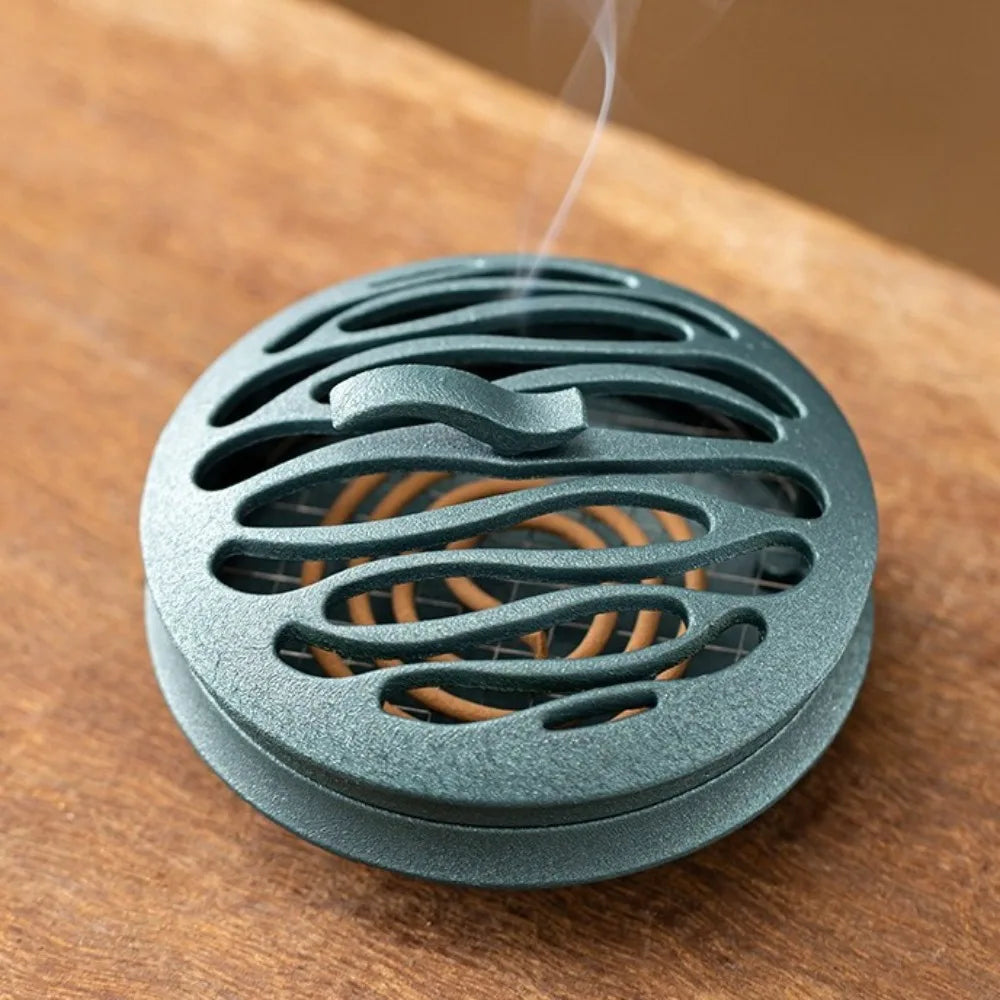 Teal/blue round incense burner close-up with curved cutout openings and smoke