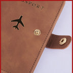 Brown passport folio cover with airplane emblem, round snap, and stitched edges detail