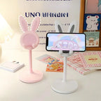 Blush pink rabbit phone stand with raised arm holding a phone; pearl white stand beside it