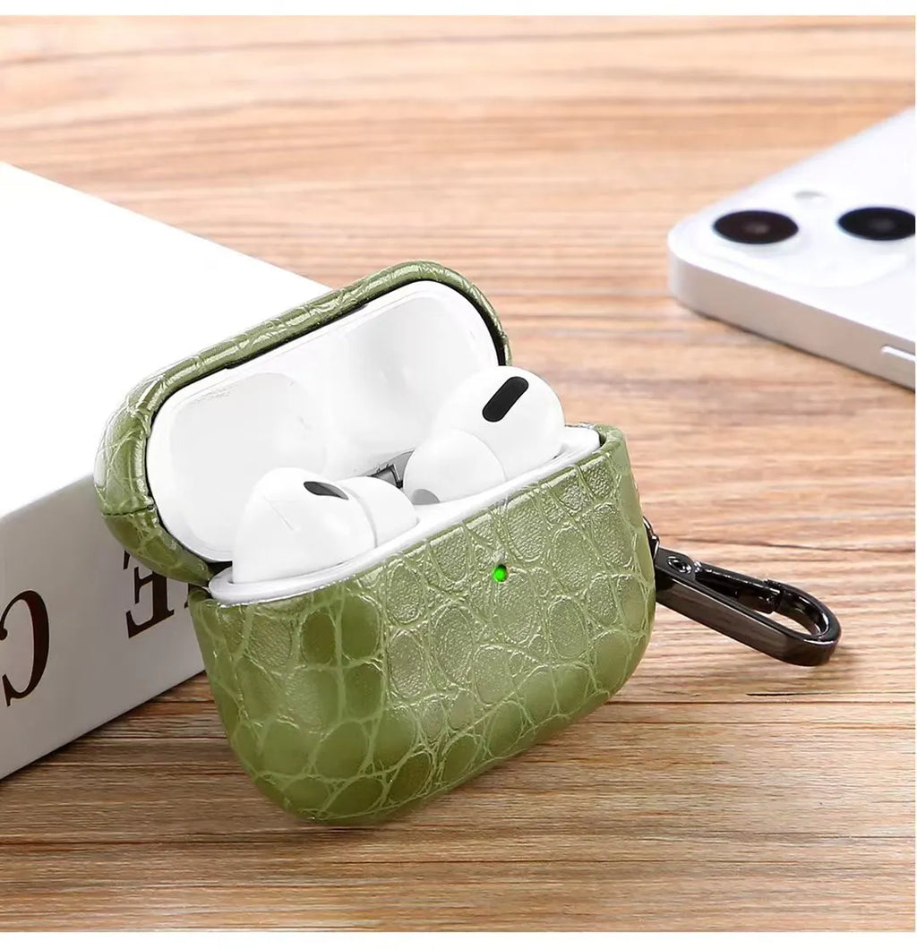 Emerald green crocodile-grain AirPods case open, earbuds inside, keychain attached.