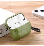 Emerald green crocodile-grain AirPods case open, earbuds inside, keychain attached.