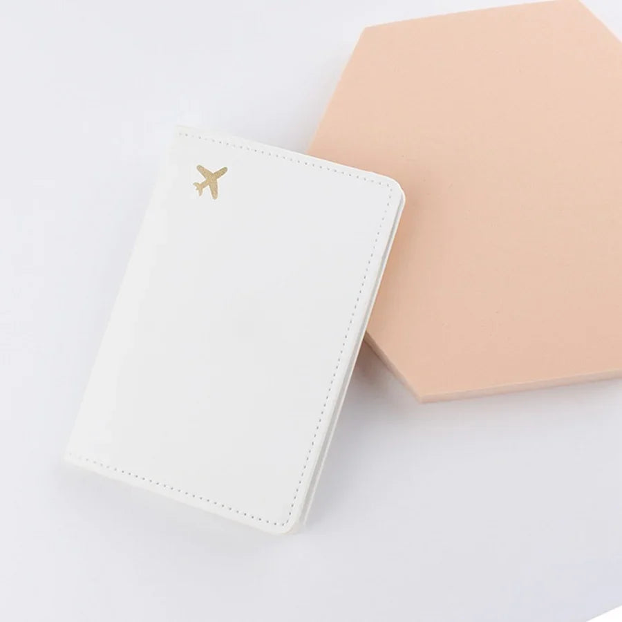 Ivory white passport sleeve with stitched edges and gold plane logo