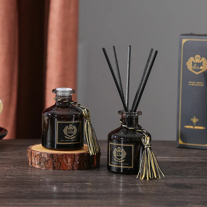 Reed diffuser bottles on wood slice, dark glass with black reeds and gold tassel ties