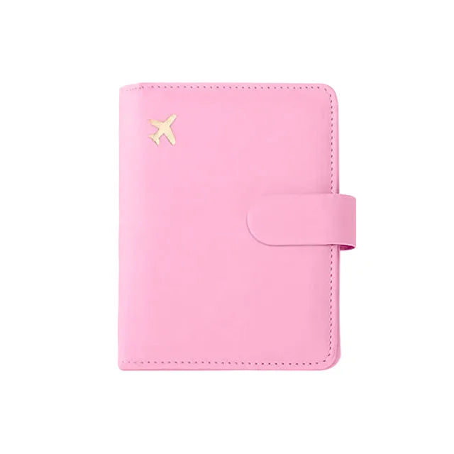 Pink passport folio with stitched border, airplane emblem, and snap strap closure