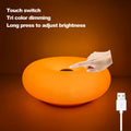 Orange glowing donut table lamp with USB charging cable connected.