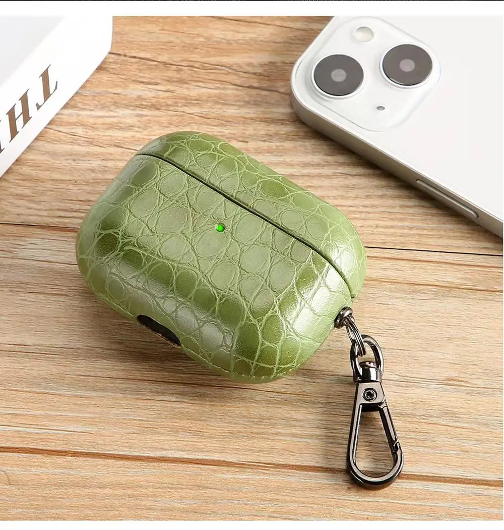 Olive green crocodile-grain AirPods case with keyring on wooden surface