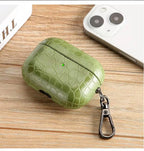 Olive green crocodile-grain AirPods case with keyring on wooden surface