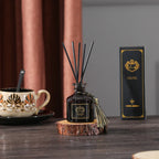 Dark glass reed diffuser bottle with black reeds and gold tassel on wood coaster