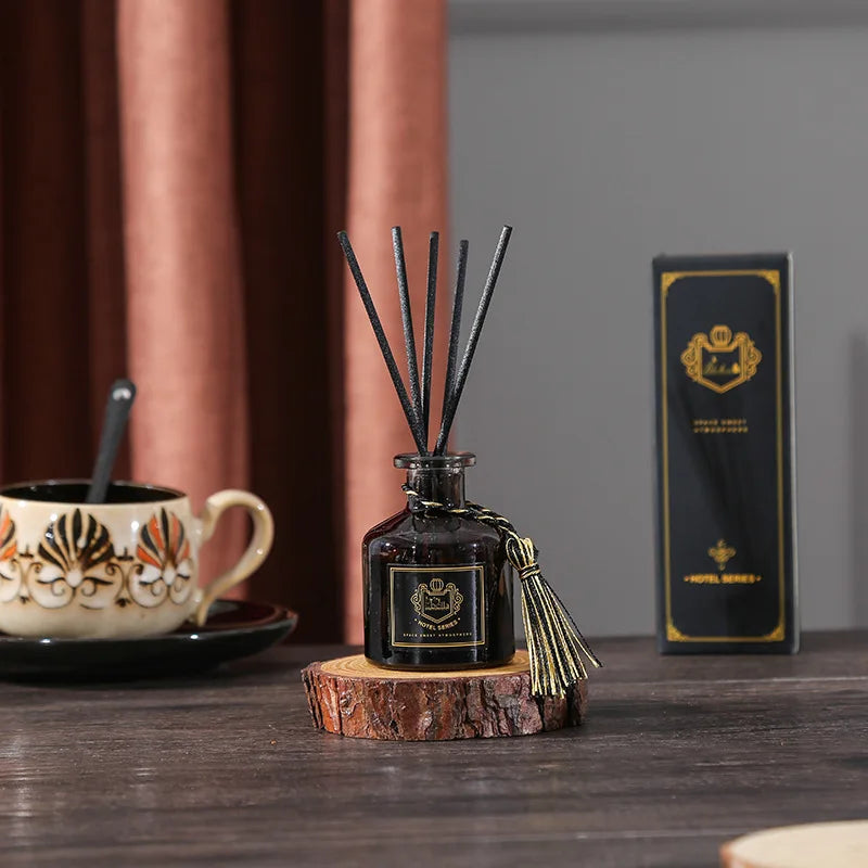 Dark glass reed diffuser bottle with black reeds and gold tassel on wood coaster