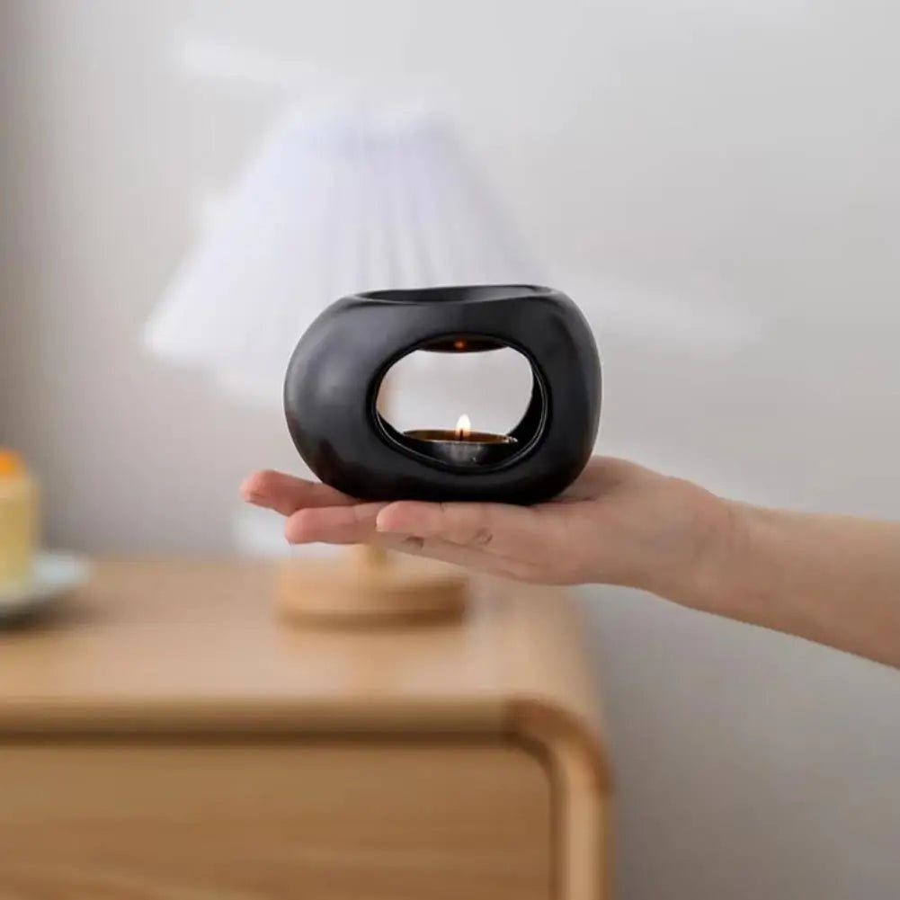 Black ceramic aroma oil burner held in hand, with window and lit candle