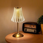 Cordless table lamp with pleated glass shade and gold base on round wooden side table