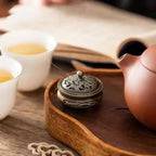 Incense plate burner with lid on a wooden tray; hand adjusts the small round cover