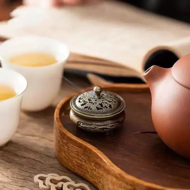 Incense plate burner with lid on a wooden tray; hand adjusts the small round cover