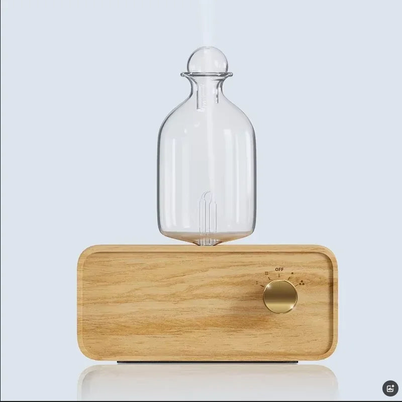 Essential oil diffuser with clear glass bottle on light wood base, power dial visible