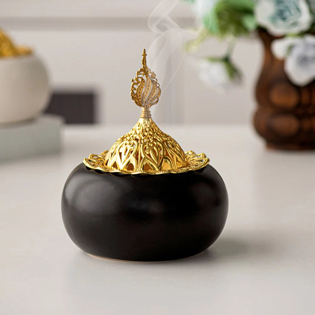 Ceramic oud burner with black dome base, gold openwork lid, visible incense smoke