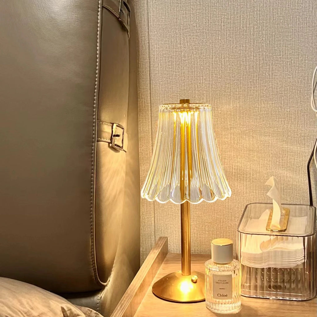 Cordless table lamp near upholstered headboard, pleated glass shade on gold base