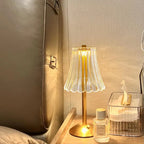 Cordless table lamp near upholstered headboard, pleated glass shade on gold base