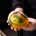 Amber glass incense vessel held in hand, ornate lid with smoke