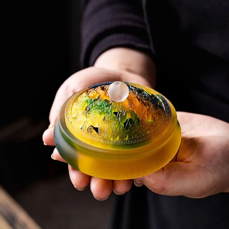 Amber glass incense vessel held in hand, ornate lid with smoke